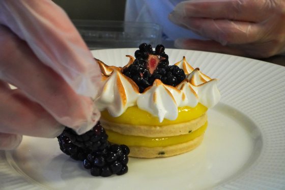 someone placing blackberries around a lemon meringue cookie tart